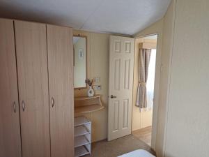 a bedroom with white cabinets and a mirror and a door at Happy Days Seaside Trusthorpe in Trusthorpe