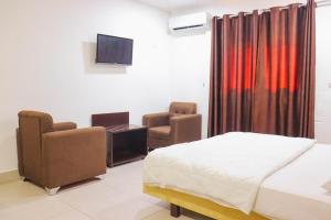 ein Schlafzimmer mit einem Bett und zwei Stühlen und einem Fernseher in der Unterkunft Brazza Hôtel in Brazzaville