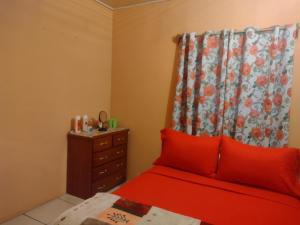 a bedroom with a red bed with a dresser and a curtain at Tessa's Inn in Arima