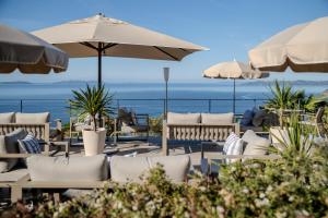 a patio with chairs and umbrellas and the ocean at Hôtel La Villa Douce in Rayol-Canadel-sur-Mer
