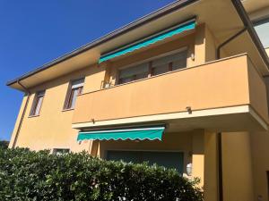 a tan building with a balcony and a blue an awning at Casa Primavera in Cinquale