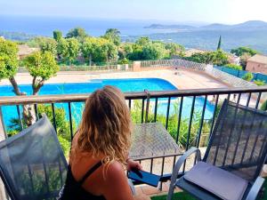 uma mulher sentada na varanda olhando para uma piscina em STUDIO POOL HOUSE MDT 2 ETOILES VUE MER PANORAMIQUE AMAZING SEA VIEW WIFI LINGE LINEN INCLUT AIRCONDITIOn em La Croix-Valmer