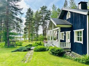 a blue house with a white porch in a yard at Blueberry Villa at Saimaa Lakeside in Taipalsaari