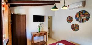 a living room with a table and a tv on the wall at Portal Suítes Casa do Lago in Paraty