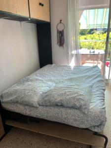 a bed with a blue comforter in a room with a window at Joana's House in La Grande-Motte