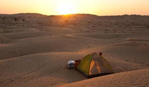 a tent in the middle of a desert with the sunset at ama in Ismant