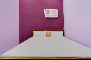 a bed with white sheets and a purple wall at Hotel O Chaudhary Hotel in Tatārpur