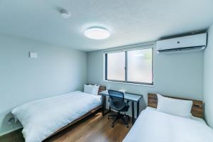 ein Zimmer mit zwei Betten und einem Schreibtisch und einem Fenster in der Unterkunft Flower Base Botan in Fukuoka