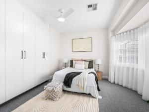 a white bedroom with a bed and a rug at Coastal Dream BeachFront Oasis in Newcastle