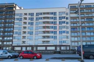a large apartment building with cars parked in a parking lot at En Bord de Mer in Middelkerke