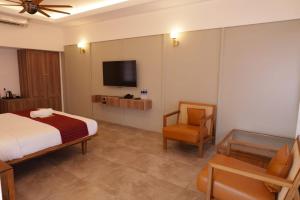 une chambre avec un lit, une télévision et une chaise dans l'établissement Arabian Pearl Beach Resort Cherai, à Cochin 2 autres photos