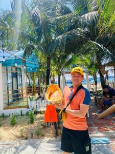 un uomo che tiene una fetta di pane accanto a una palma di Villa Hoàng Diệu Phú Quý 260m2 có bãi tắm trước nhà a Cù Lao Thu Altre 5 foto