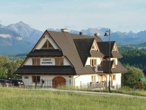 a house with a black roof with mountains in the background at Chata Koziniec przy wyciągu in Czarna Góra