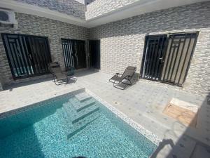 a swimming pool with two chairs and a house at Résidence Codou Bigué in Ouayembame