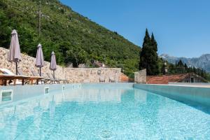 a swimming pool with umbrellas and a mountain at GuestHouse Mrshe Palace in Perast