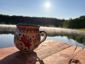 a coffee cup sitting on a table next to a body of water at Domek Rogalewo in Wiele