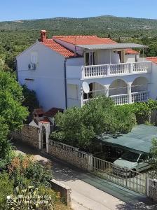 a white house with a balcony and a fence at Apartmani Uvodić in Rogoznica