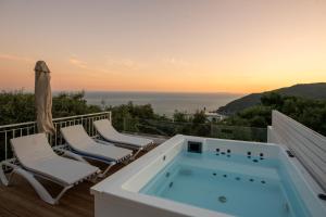 a hot tub on a deck with chairs and the ocean at Elaia's Villas Hot Tub & Seaview in Parga