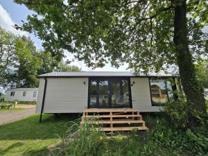 a tiny house with a porch and a tree at Tiny House Drents-Friese Wold in Hoogersmilde
