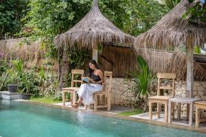 a woman sitting at a table next to a swimming pool at Golden Garuda Cottages at Diamond Beach Hills in Nusa Penida