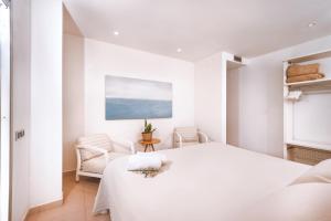 a white bedroom with a bed and two chairs at Apartamentos Porta Coeli in Castelldefels +59 photos