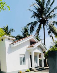 a white house with a palm tree in the background at Lima Blue Private Beach Apartment in Trincomalee