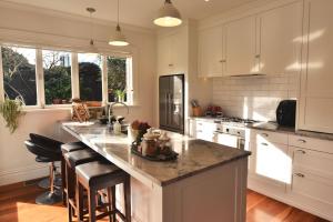 a kitchen with white cabinets and a large island with bar stools at Welcome to Blue Morning house! - Remuera 5 bedrooms villa in Auckland