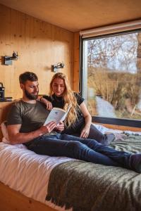 Ein Mann und eine Frau sitzen auf einem Bett mit einem Buch in der Unterkunft Parcel Tiny House Péa au coeur de la Loire in Saint-Marcel-dʼUrfé