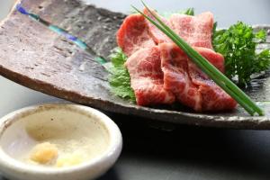 a plate of food with meat and a bowl of dipping sauce at Minshuku Asogen in Aso