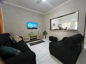 ein Wohnzimmer mit einem schwarzen Sofa und einem Flachbild-TV in der Unterkunft Casa de 2 Quartos à 5 min a Pé da Praia, com Churrasqueira e 3 Vagas de Garagem in Praia Grande