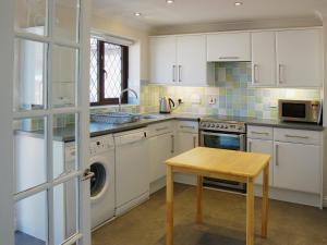 パドストウにあるSea Whispersの白いキャビネットと木製のテーブルのあるキッチン