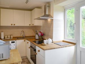 a kitchen with white cabinets and a sink and a window at Winscott Cottage in Pyworthy
