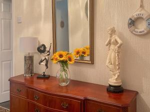 une commode avec un vase de fleurs et une statue dessus dans l'établissement The Bay Cottage, à Thornton