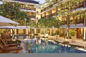 a hotel with a swimming pool with trees and chairs at The Rani Hotel & Spa in Kuta