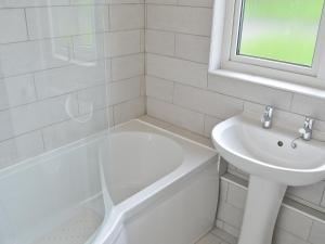 a white bathroom with a sink and a tub and a toilet at Eider Cottage in Embleton