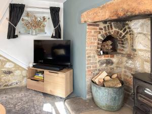 a living room with a tv and a brick fireplace at Winkle Cottage in Calbourne