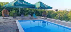 a swimming pool with two umbrellas and chairs next to at Vikendica Elenda Banja Luka in Laktaši