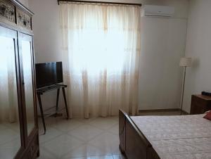 Un dormitorio con una cama y una ventana con un televisor. en Villa Marissimo, en Realmonte