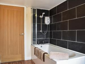 a bathroom with a bath tub with black tiles at Winnies Cottage in Belford