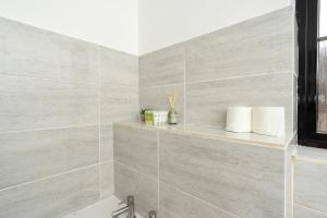 a bathroom with gray tile walls and a shelf with towels at Open Mind Property - Cozy 2 Bed Room & Free Parking in Portsmouth