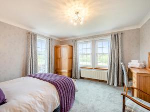 a bedroom with a bed and a desk and windows at Kerrytonlia Cottage in Mountstuart