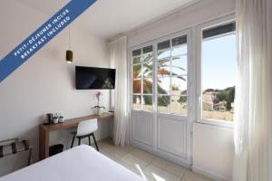 a bedroom with a bed and a desk and a window at Hôtel Les Voiles in Toulon