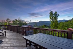 a wooden deck with a table and chairs and mountains at Whiskey Hills - Newly Remodeled Luxury Cabin with Hot Tub, Incredible Views close to Asheville, walk to Hatley Pointe & Ski! in Swiss