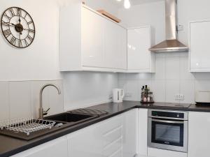 a kitchen with white cabinets and a clock on the wall at Katellen Cottage in Threlkeld