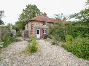 a brick house with a white door in a garden at Broom Cottage in East Rudham