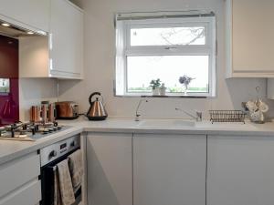 una cucina bianca con lavandino e finestra di Honeysuckle Cottage a Springside Altre 12 foto
