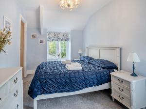 a bedroom with a bed with a blue comforter and a window at Miners Arms Cottage in Stepaside