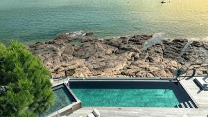 a swimming pool next to the ocean with a rock formation at Hôtel Castel d'Orcino in Calcatoggio