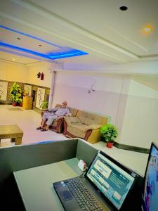 a man sitting on a couch in a room with a laptop at AL AQSA SUiTES Guest House Islamabad in Islamabad