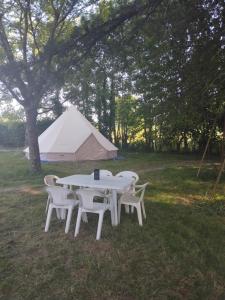 Saint-MesminLogement atypique的田野里有一张白色的桌子和几把椅子，还有一顶帐篷
